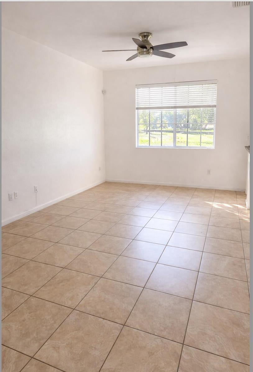 An empty room with beige tile flooring, white walls, a ceiling fan, and a window — 1219 Lucaya Drive, Riviera Beach FL 33404, RIVIERA BEACH, FL