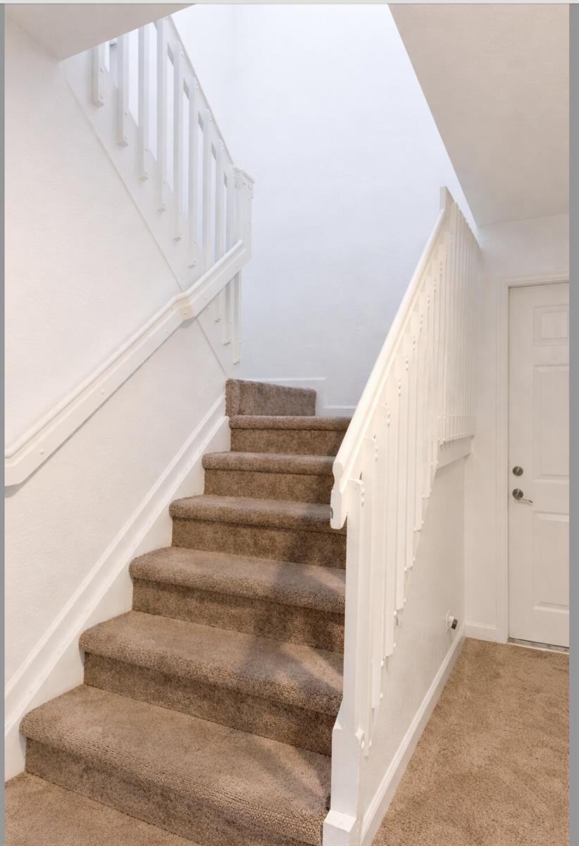 A carpeted staircase with white railings leads upward in a bright, minimalist entryway — 1219 Lucaya Drive, Riviera Beach FL 33404, RIVIERA BEACH, FL