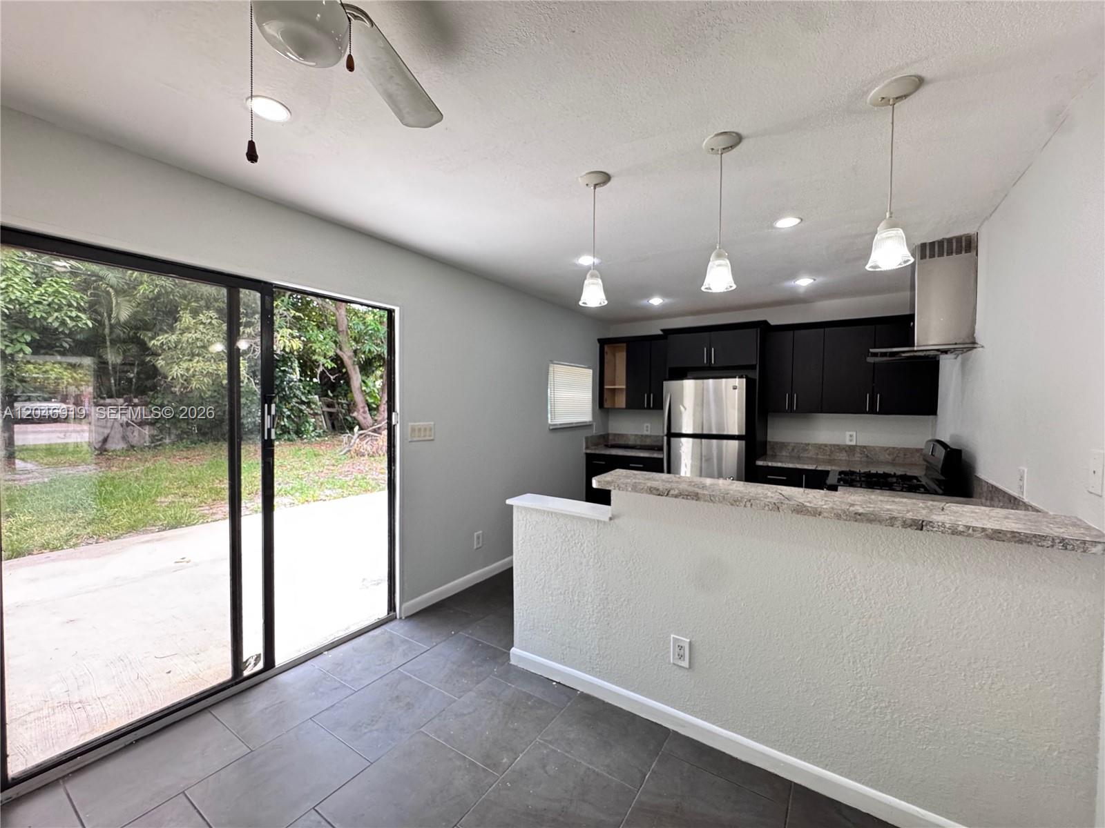A kitchen with dark cabinets, stainless steel appliances, and a breakfast bar overlooks a yard — 1801 NE 50th St, Pompano Beach FL 33064, POMPANO BEACH, FL