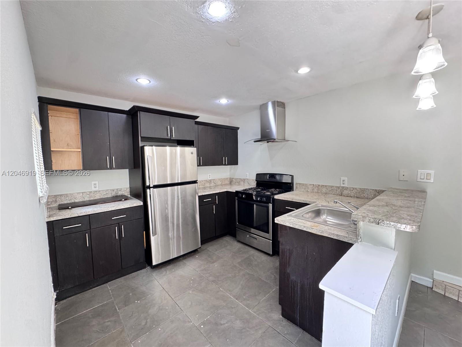 A kitchen features dark cabinets, stainless steel appliances, granite countertops, and gray tile flooring — 1801 NE 50th St, Pompano Beach FL 33064, POMPANO BEACH, FL