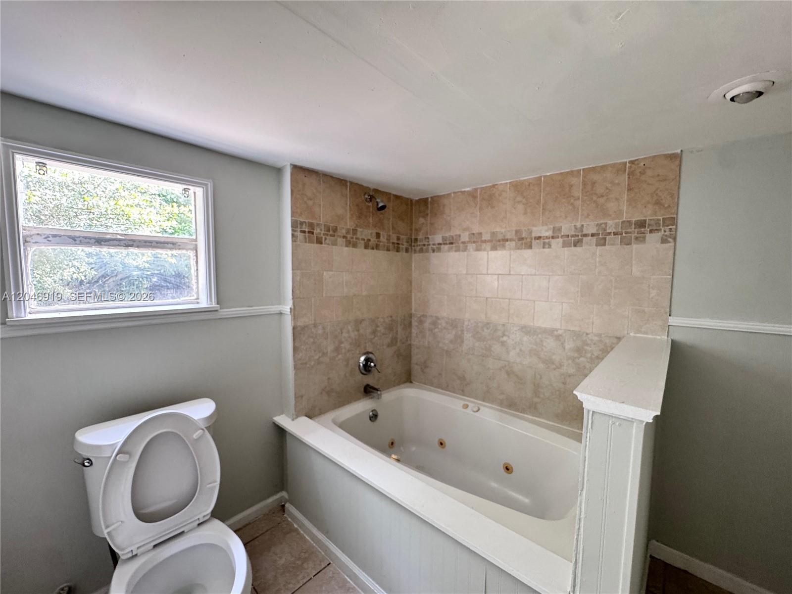 A bathroom features a jetted tub with tiled walls, a toilet, and a window — 1801 NE 50th St, Pompano Beach FL 33064, POMPANO BEACH, FL