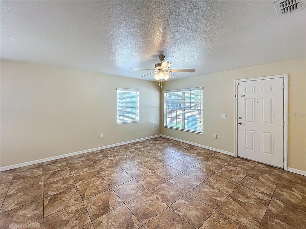An empty room features tan walls, brown tile flooring, a ceiling fan, and a front door — 838 N IOWA AVENUE, LAKELAND, FL
