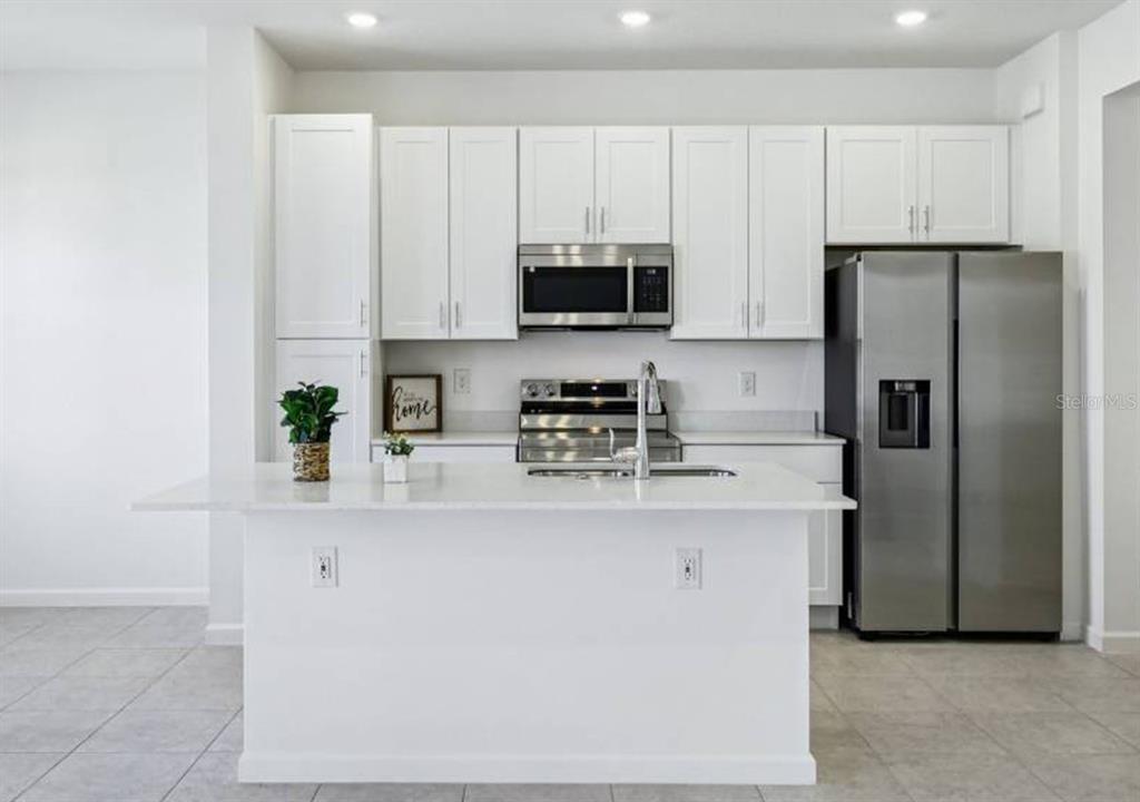 A modern kitchen features white cabinets, stainless steel appliances, and a central island with seating — 24101 MANUMA STREET UNIT Seminole 2491, ST CLOUD, FL