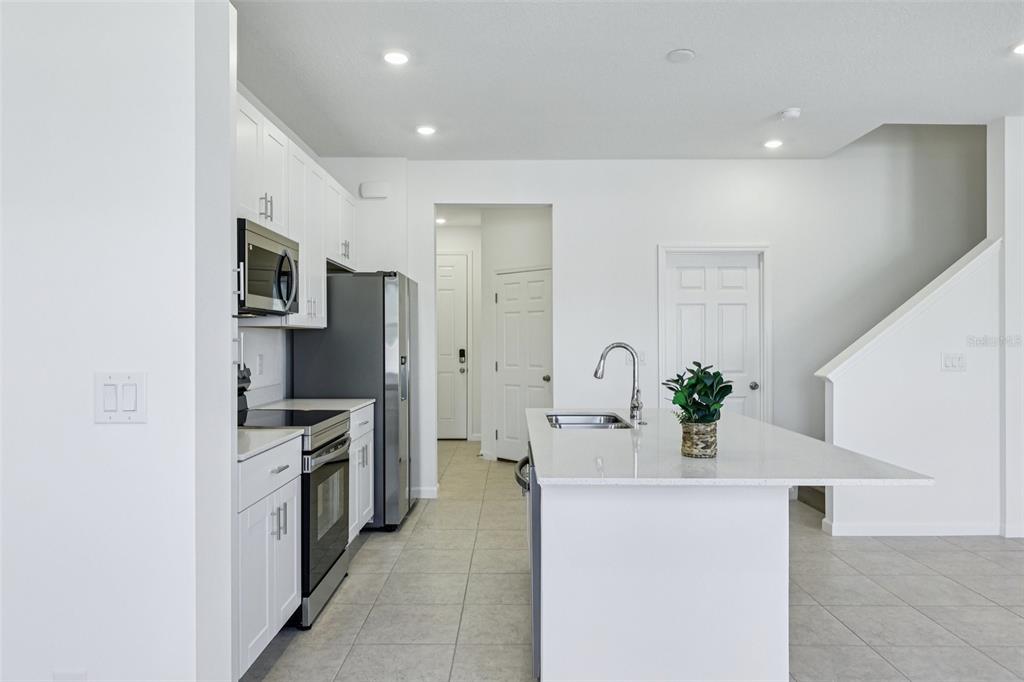 A modern kitchen features white cabinetry, stainless steel appliances, a center island, and tile flooring — 24101 MANUMA STREET UNIT Seminole 2491, ST CLOUD, FL