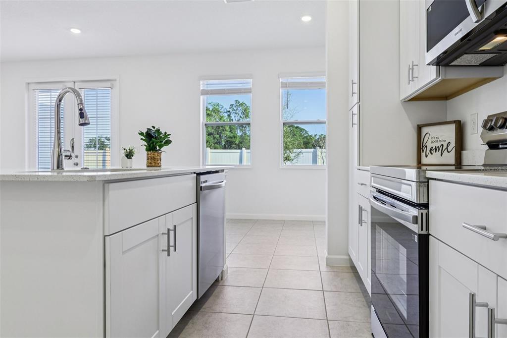 A modern kitchen features white cabinets, stainless steel appliances, a center island, and tiled floors — 24101 MANUMA STREET UNIT Seminole 2491, ST CLOUD, FL