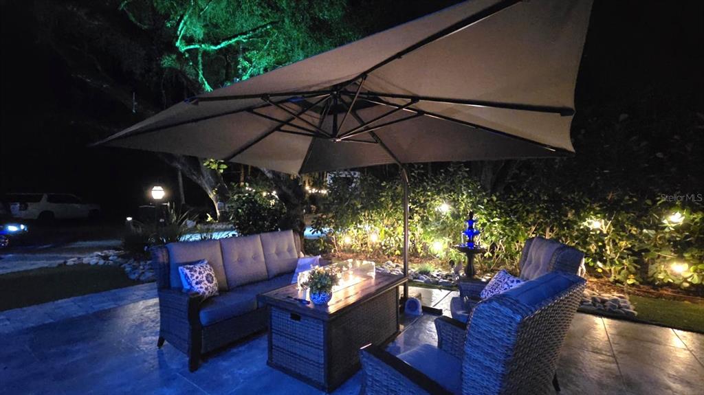 An outdoor patio at night features a sofa, chairs, and a fire pit under an umbrella — 422 LONGHORN DRIVE, LAKE WALES, FL