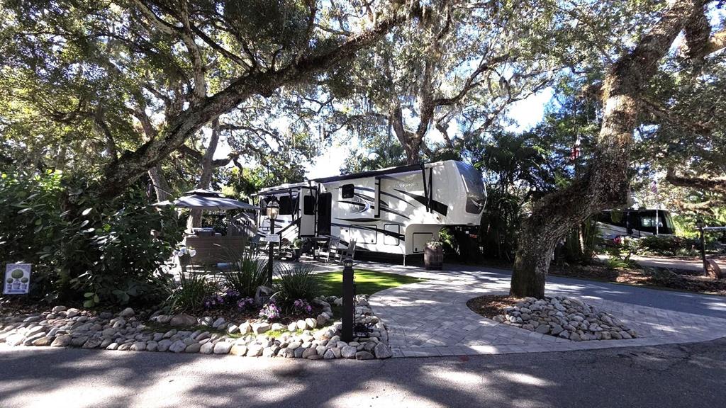 A large fifth-wheel RV is parked on a paved lot under mature oak trees — 422 LONGHORN DRIVE, LAKE WALES, FL