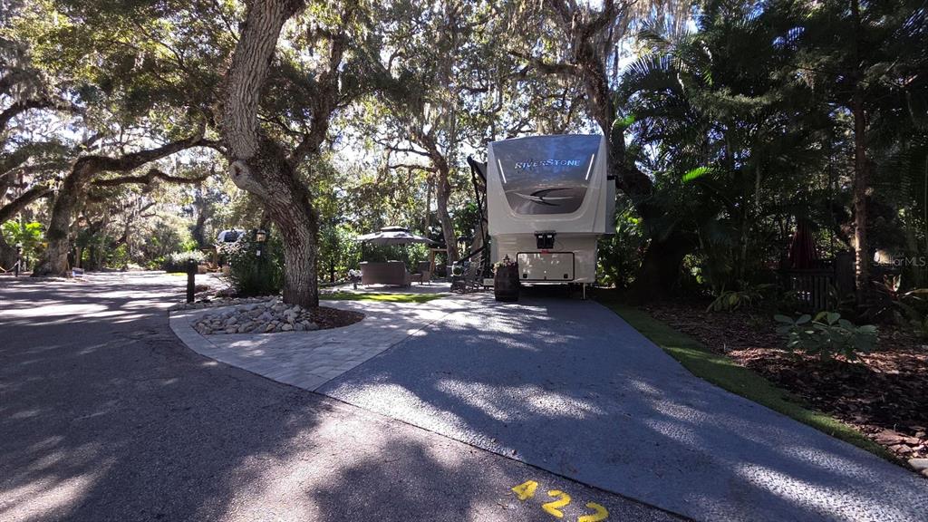 A large RV is parked on a paved lot shaded by mature trees — 422 LONGHORN DRIVE, LAKE WALES, FL