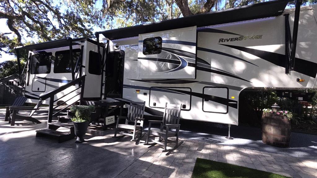 A large Riverstone fifth-wheel RV is parked on a paved patio with outdoor rocking chairs — 422 LONGHORN DRIVE, LAKE WALES, FL