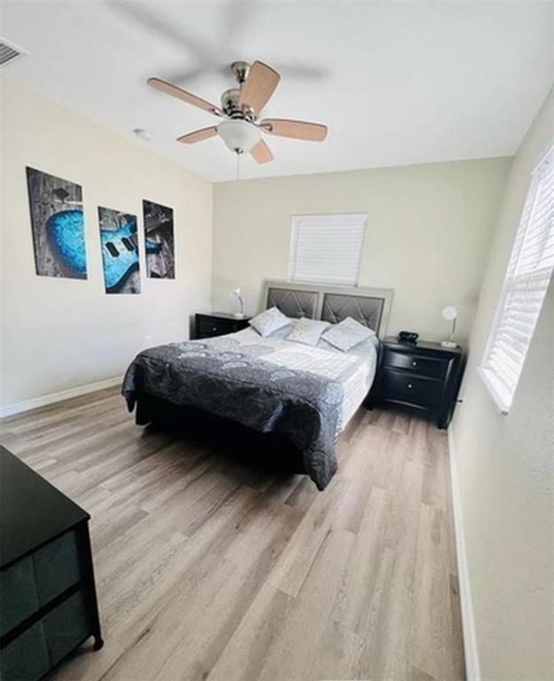 A bedroom features light wood-look flooring, a ceiling fan, and a bed with black nightstands — 1500 77TH STREET N, ST PETERSBURG, FL