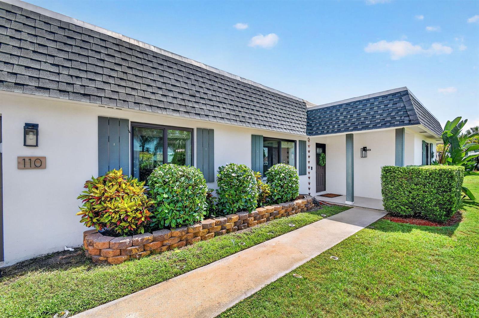 A white single-story house with a dark shingled roof, brick planter, and a concrete walkway — 110 W Coconut Drive, Lake Worth FL 33467, LAKE WORTH, FL
