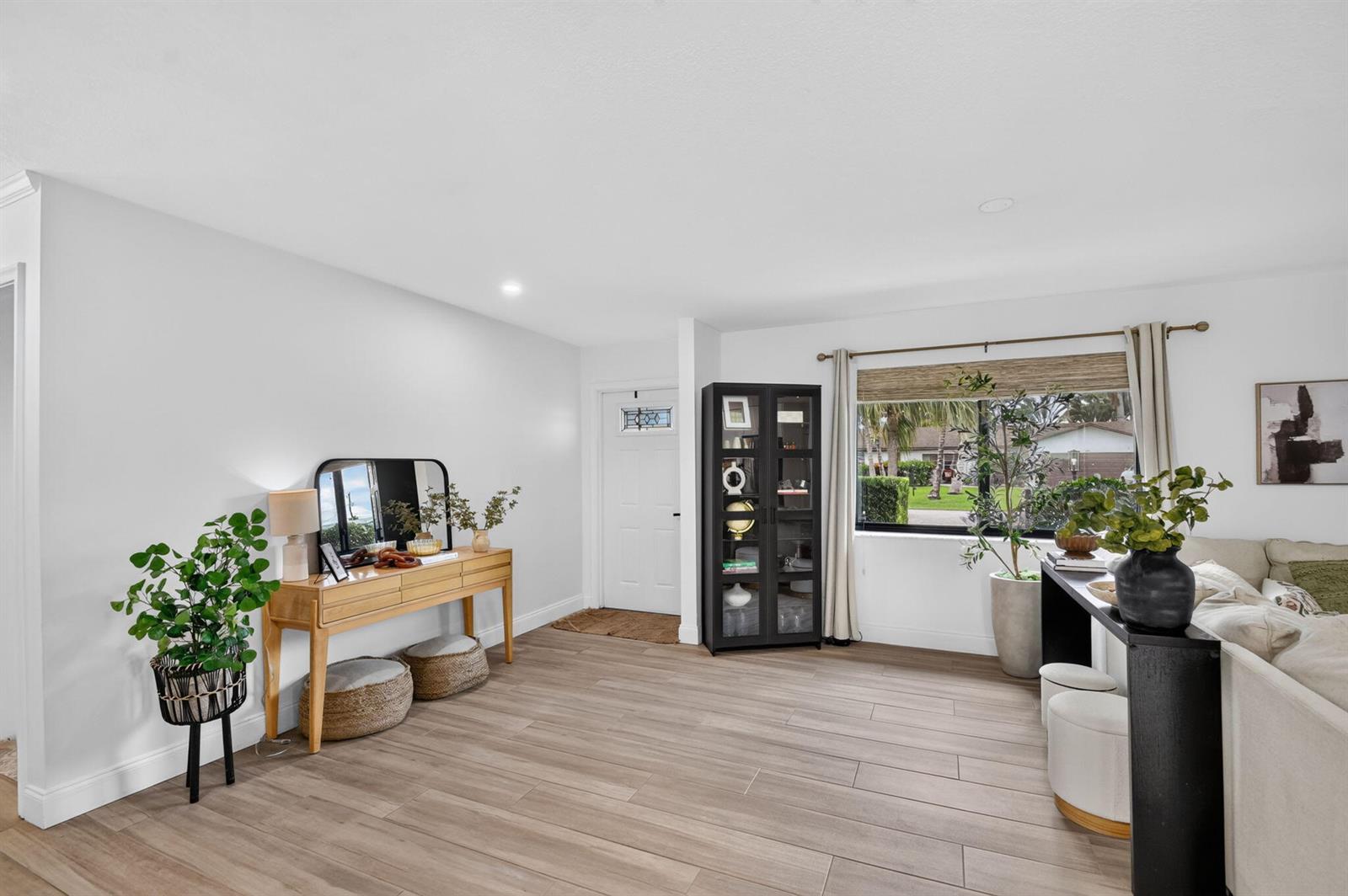 A bright living room features light wood-look tile flooring, a console table, and a display cabinet — 110 W Coconut Drive, Lake Worth FL 33467, LAKE WORTH, FL