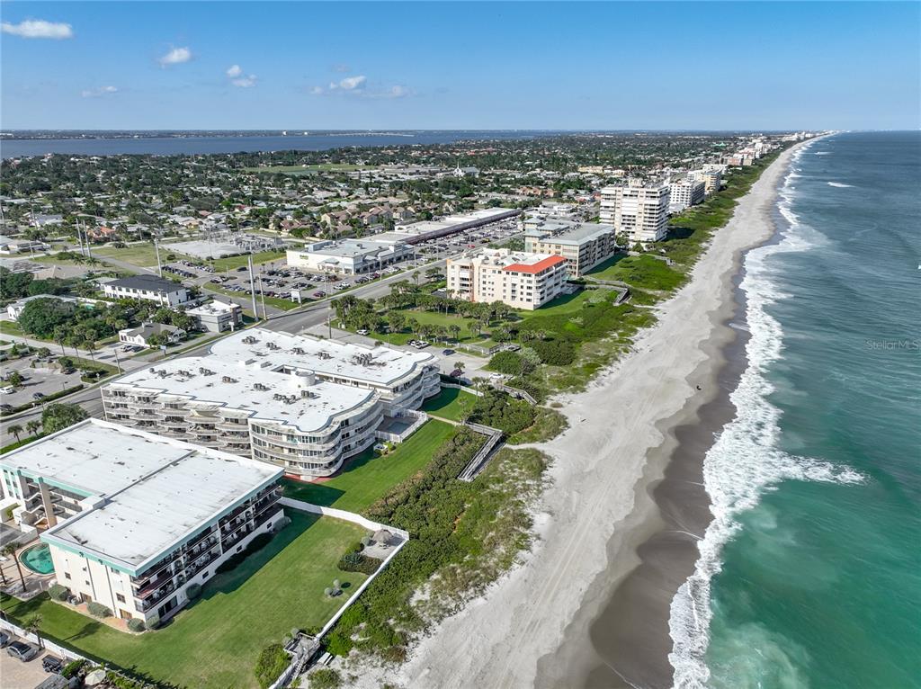 An aerial view shows beachfront condominiums, a sandy shoreline, and a coastal town — 601 N MIRAMAR AVENUE UNIT 205, INDIALANTIC, FL