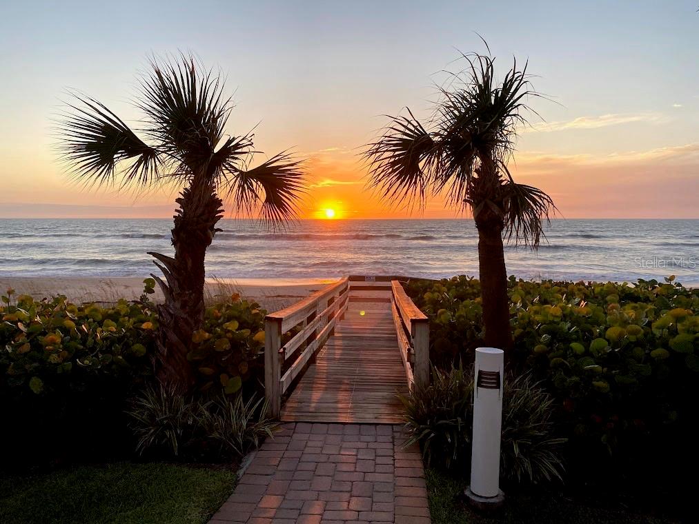 A wooden boardwalk leads through palm trees to a sandy beach at sunset — 601 N MIRAMAR AVENUE UNIT 205, INDIALANTIC, FL