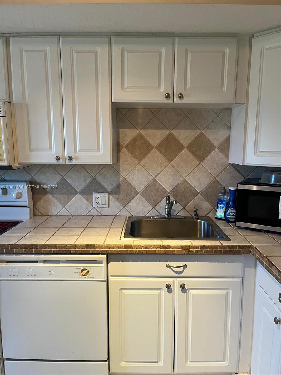 A kitchen features white cabinets, a tiled countertop, and a diamond-patterned backsplash — 3200 N Palm Aire Dr # 407, Pompano Beach FL 33069, POMPANO BEACH, FL