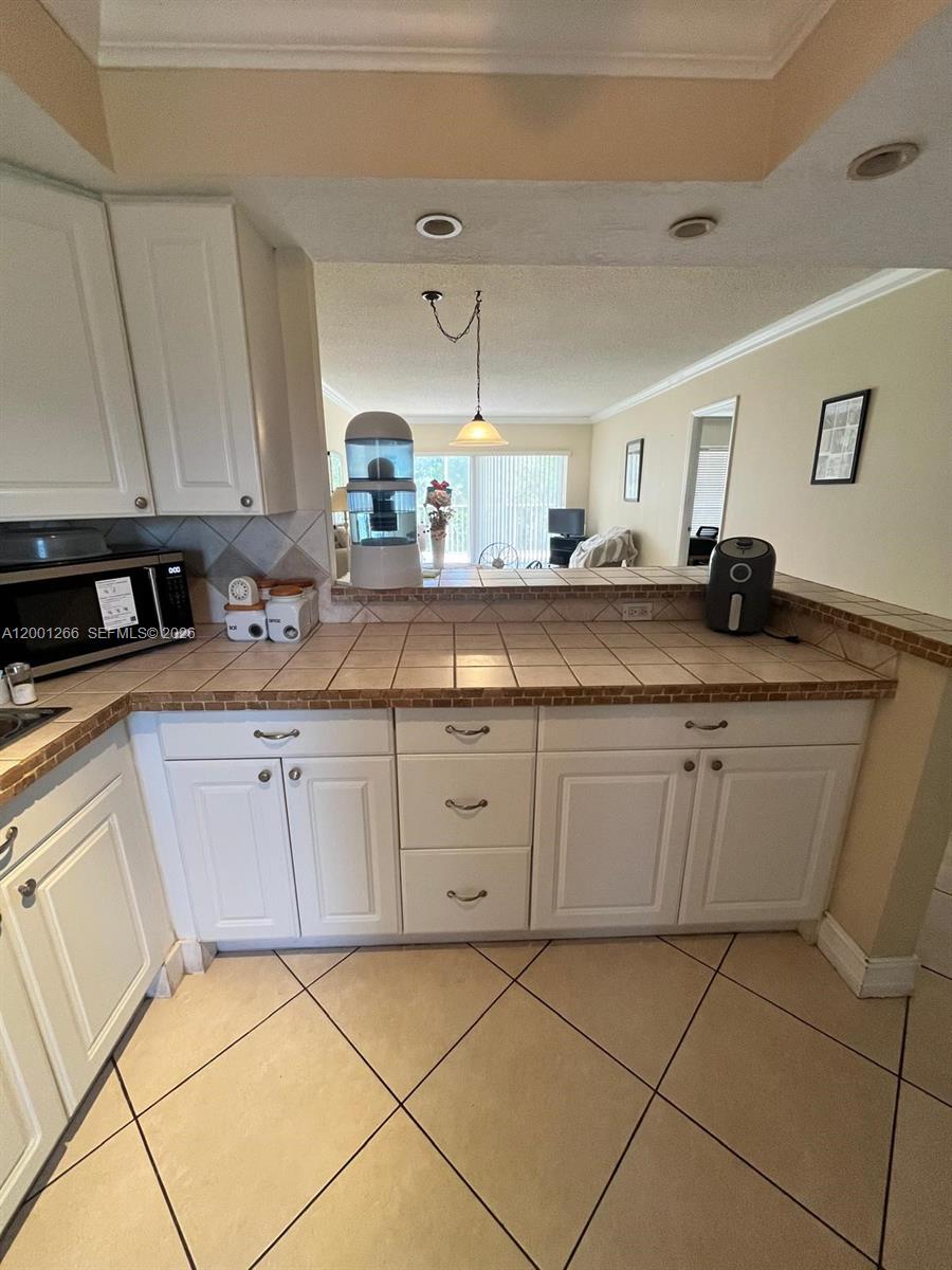 A kitchen features white cabinets, tiled countertops, and a pass-through window overlooking the living area — 3200 N Palm Aire Dr # 407, Pompano Beach FL 33069, POMPANO BEACH, FL