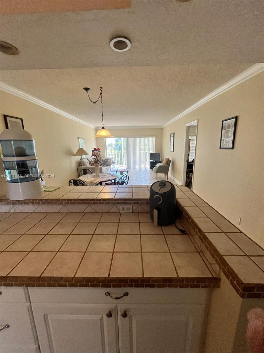 A kitchen counter with tile finishes overlooks a living and dining area with balcony access — 3200 N Palm Aire Dr # 407, Pompano Beach FL 33069, POMPANO BEACH, FL