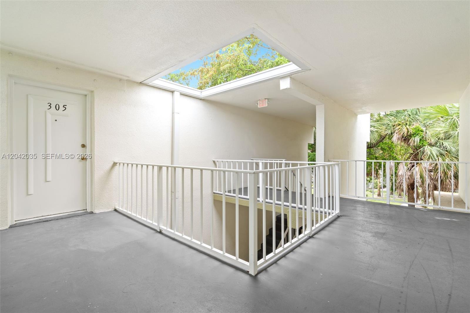 An outdoor apartment hallway features a white door, a skylight, and a metal railing — 4215 N University Dr # 305, Sunrise FL 33351, SUNRISE, FL