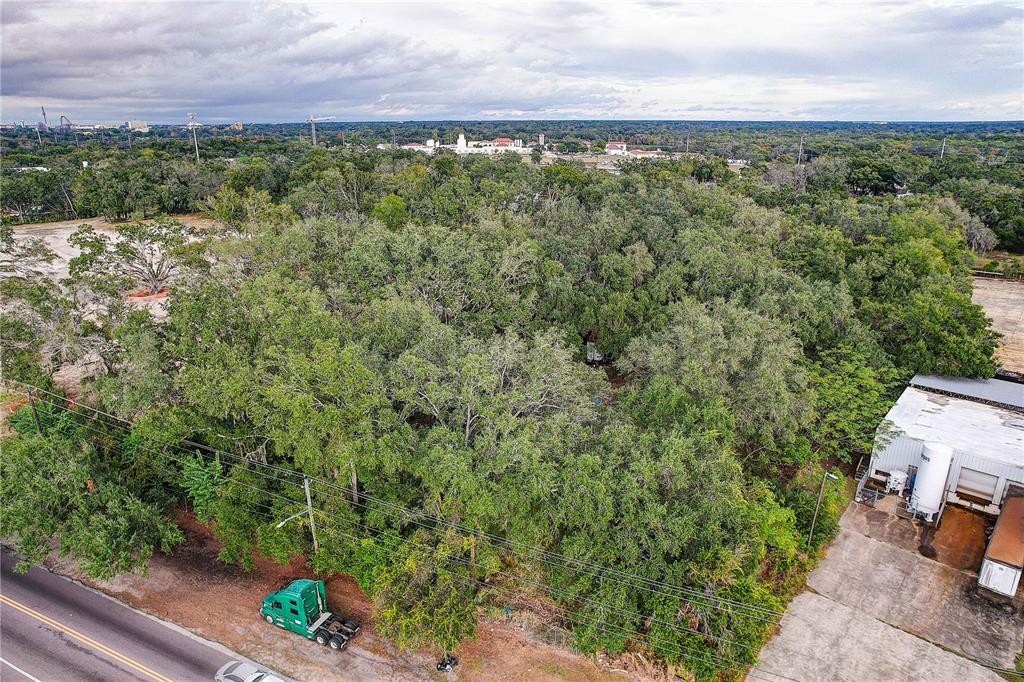 An aerial view shows a wooded lot situated between a road and a commercial building — 6905 & 6907 ROWLETT PARK DRIVE, TAMPA, FL