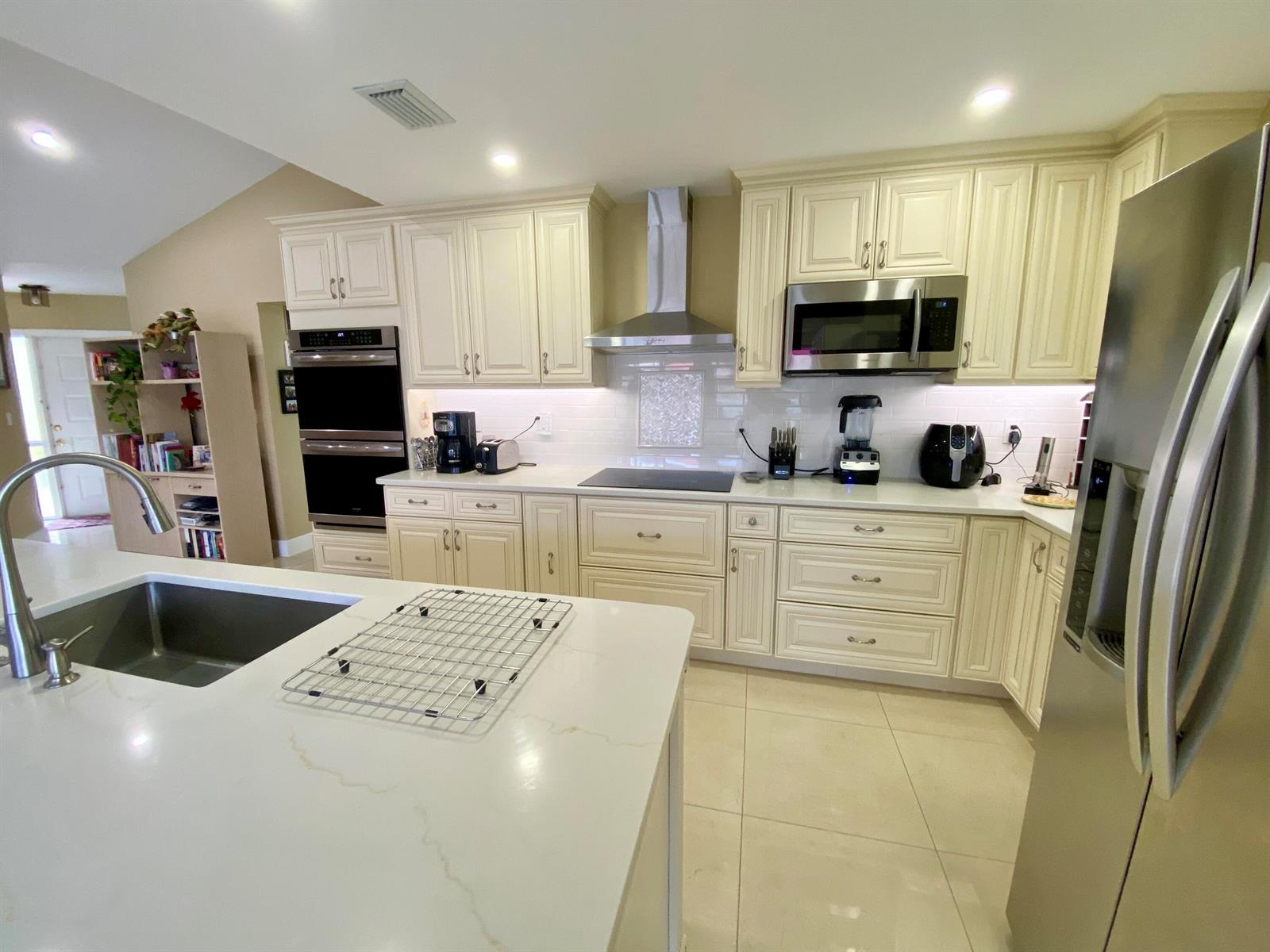 A modern kitchen features cream-colored cabinets, stainless steel appliances, and a large white island — 1127 E Seminole Avenue # 13d, Jupiter FL 33477, JUPITER, FL