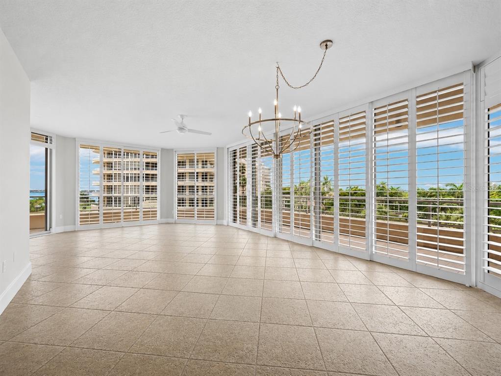 A bright, tiled living room features a chandelier, ceiling fan, and floor-to-ceiling plantation shutters — 3040 GRAND BAY BOULEVARD UNIT 225, LONGBOAT KEY, FL