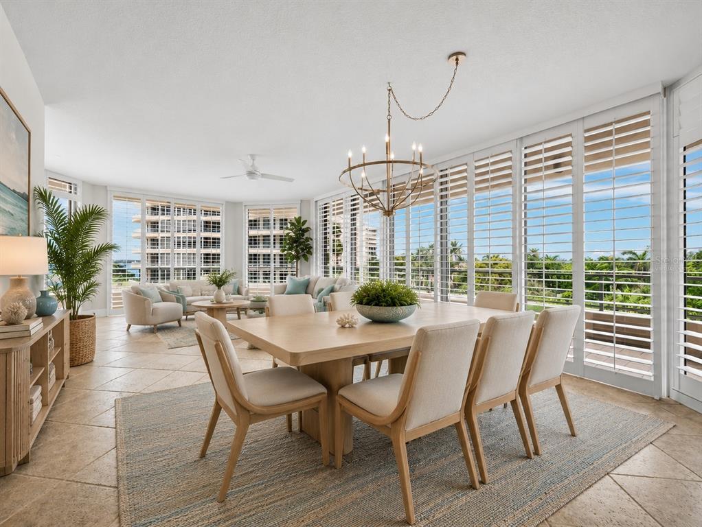 A dining area with a wooden table and chairs sits before floor-to-ceiling windows with shutters — 3040 GRAND BAY BOULEVARD UNIT 225, LONGBOAT KEY, FL
