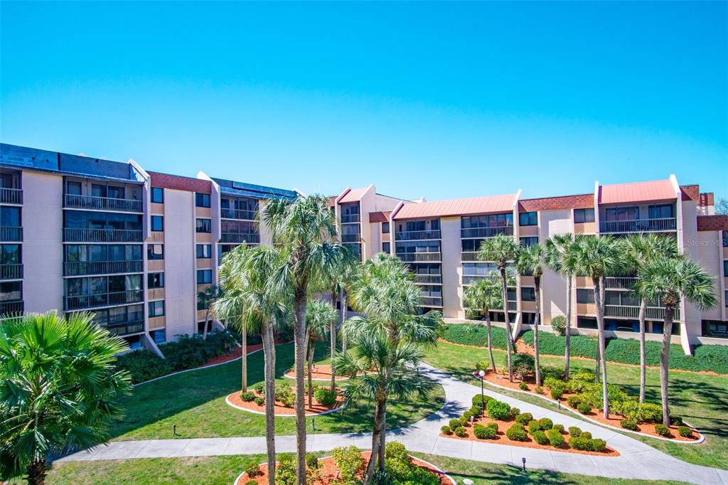 An exterior view of a multi-story apartment complex with palm trees and a paved walkway — 3006 CARING WAY UNIT 523, PORT CHARLOTTE, FL