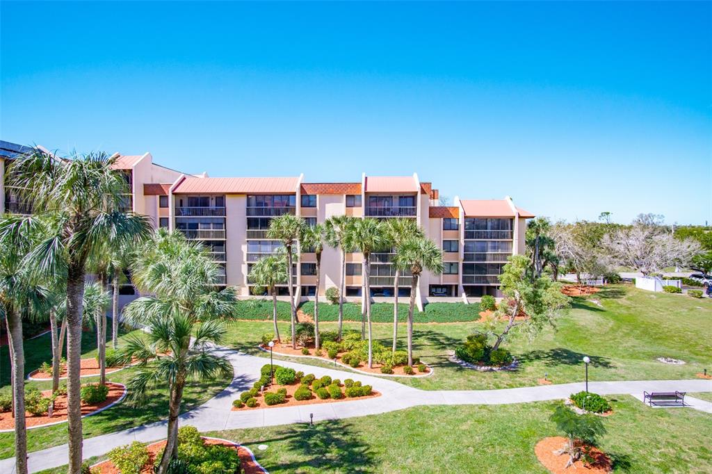 An exterior view of a multi-story apartment building with palm trees and a landscaped courtyard — 3006 CARING WAY UNIT 523, PORT CHARLOTTE, FL
