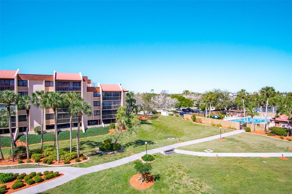 An exterior view of a multi-story apartment building with a lawn, pool, and palm trees — 3006 CARING WAY UNIT 523, PORT CHARLOTTE, FL