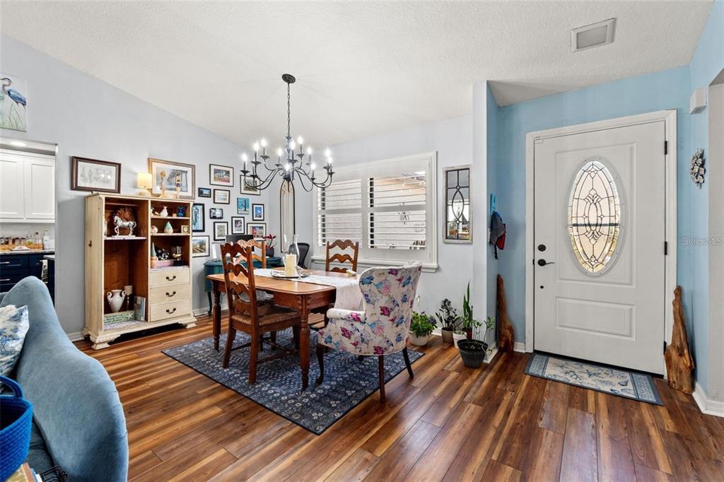 A dining area features a wooden table, floral chairs, a chandelier, and a white front door — 7427 HEATHER WALK DRIVE, WEEKI WACHEE, FL