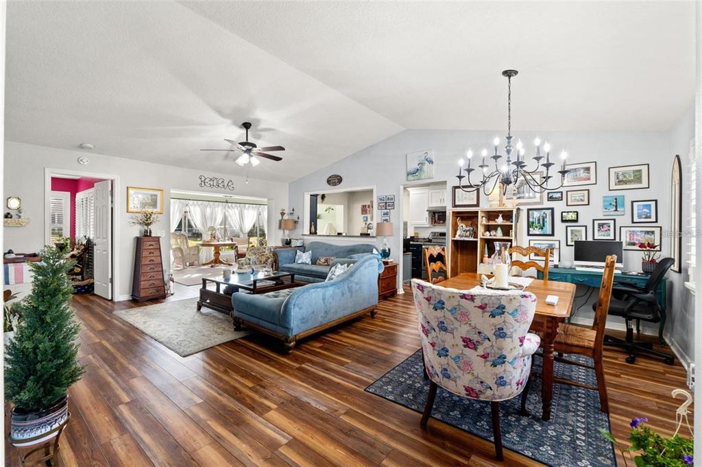 An open-concept living and dining area features wood-look flooring, a vaulted ceiling, and a chandelier — 7427 HEATHER WALK DRIVE, WEEKI WACHEE, FL
