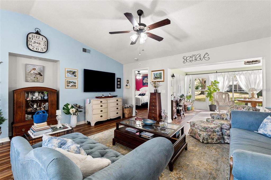 A living room features blue walls, a ceiling fan, a television, and two blue sofas — 7427 HEATHER WALK DRIVE, WEEKI WACHEE, FL