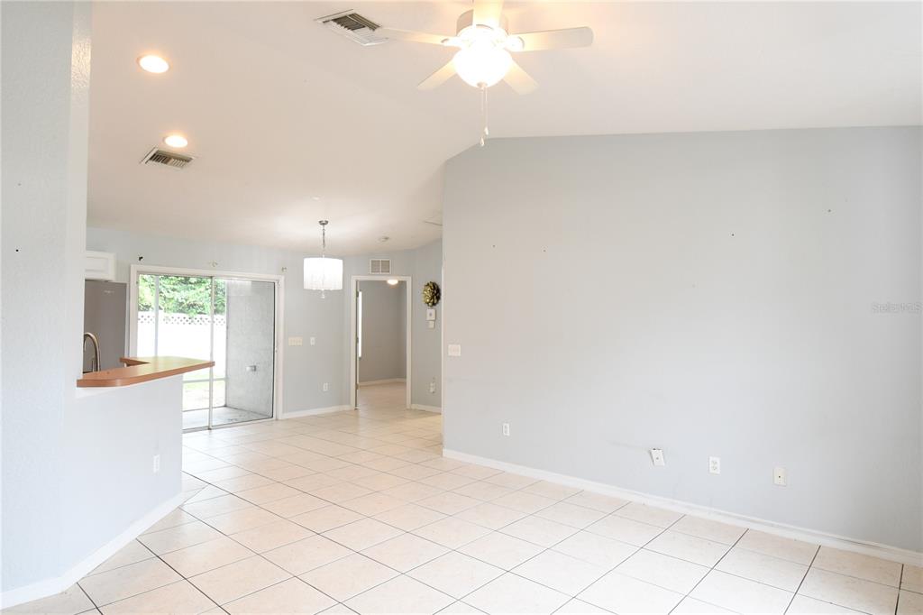 An open-concept living area features light-colored tile flooring, a ceiling fan, and a kitchen counter — 407 CIERRA OAKS CIRCLE, LADY LAKE, FL