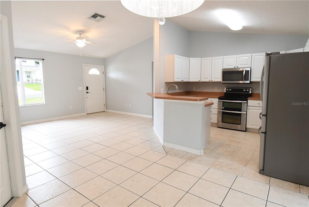 An open-concept kitchen and living area features white cabinets, stainless steel appliances, and tile flooring — 407 CIERRA OAKS CIRCLE, LADY LAKE, FL