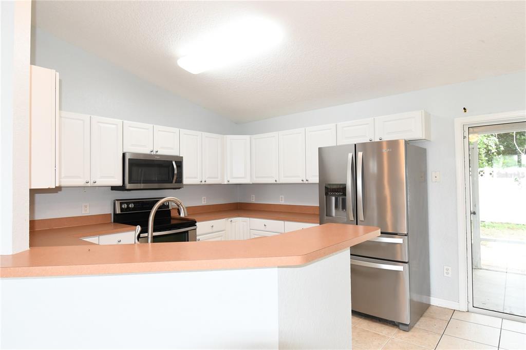 A kitchen with white cabinets, a stainless steel refrigerator, and a tan laminate countertop — 407 CIERRA OAKS CIRCLE, LADY LAKE, FL