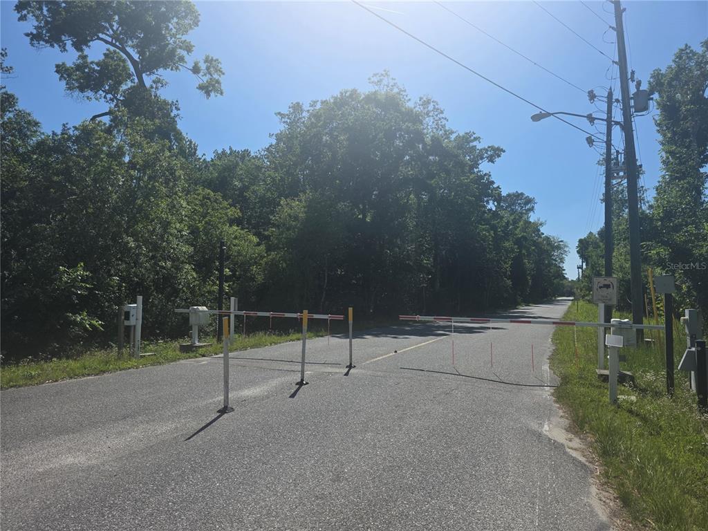 A paved road is blocked by a red and white striped security gate — 0 SWEETWATER TRAIL Lot 145, KISSIMMEE, FL