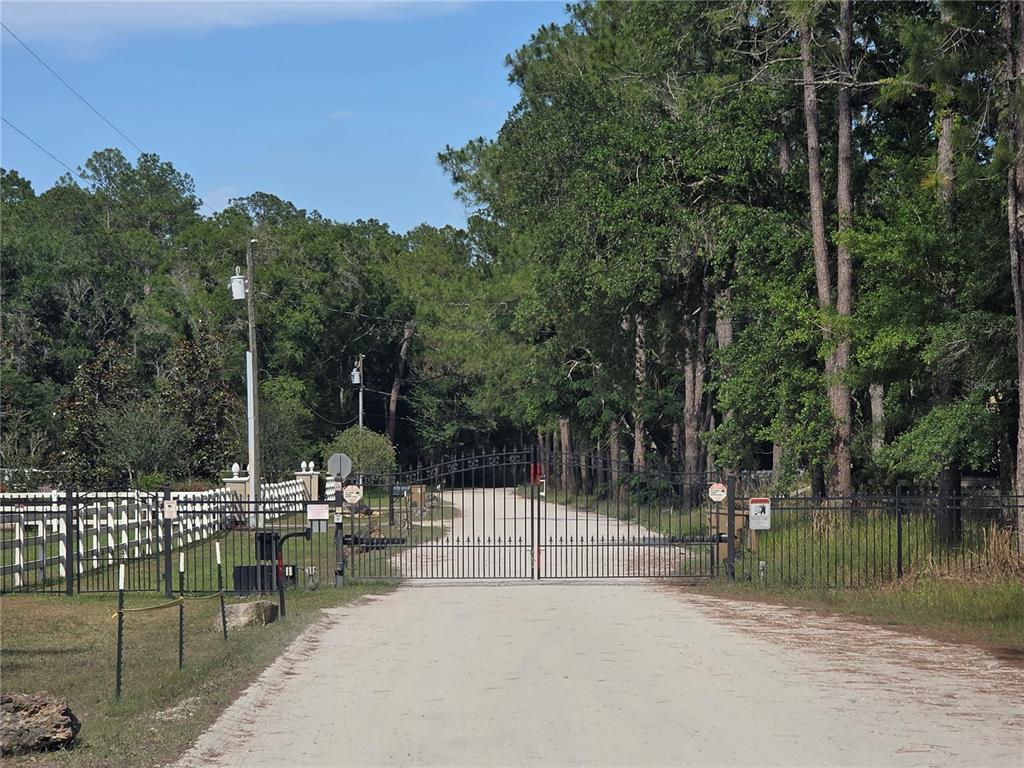 A gravel driveway leads to a gated entrance surrounded by a fence and dense trees — 0 SWEETWATER TRAIL Lot 145, KISSIMMEE, FL