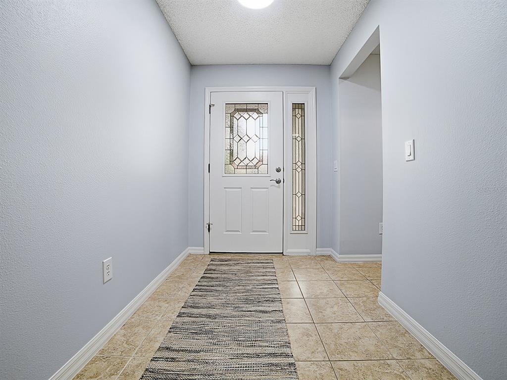 An entryway features light blue walls, a tiled floor, a runner rug, and a front door — 7290 SE 172ND LEGACY LANE, THE VILLAGES, FL