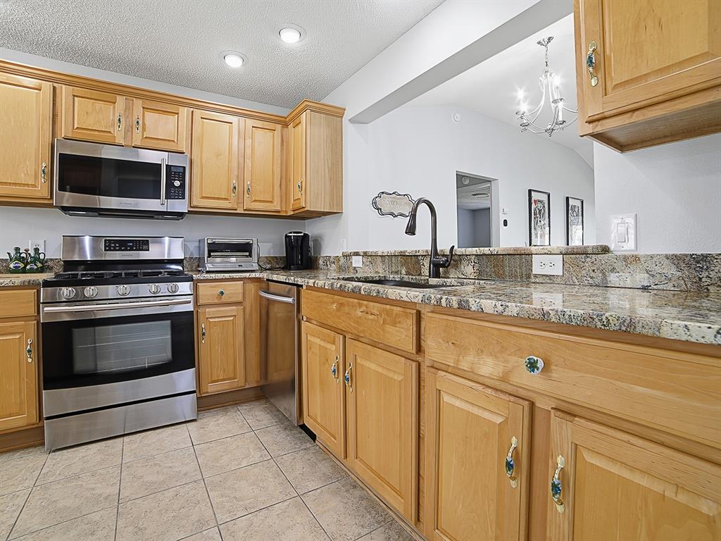 A kitchen features light wood cabinets, granite countertops, stainless steel appliances, and tile flooring — 7290 SE 172ND LEGACY LANE, THE VILLAGES, FL