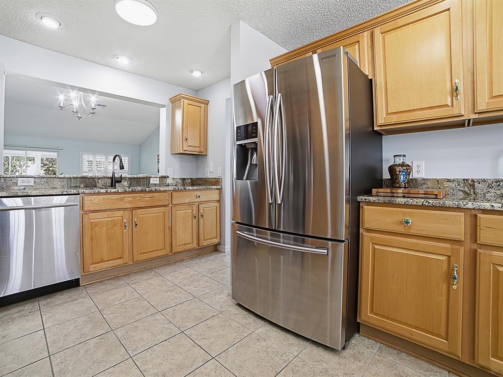 A kitchen features light wood cabinets, granite countertops, stainless steel appliances, and tile flooring — 7290 SE 172ND LEGACY LANE, THE VILLAGES, FL