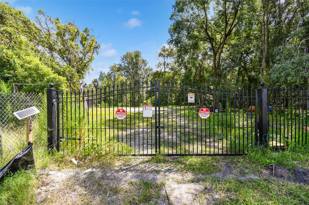 A black metal gate stands at the entrance to a wooded, fenced-in dirt lot — 1758 LAND O LAKES BOULEVARD, LUTZ, FL
