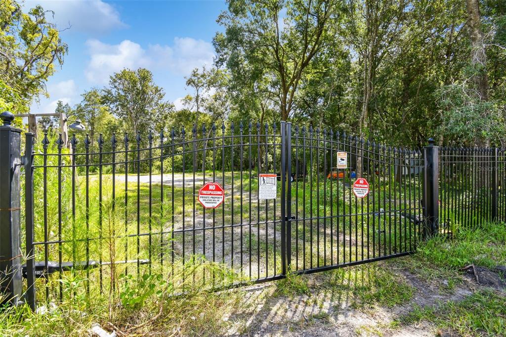 A black metal gate stands at the entrance of a wooded, fenced-in property — 1758 LAND O LAKES BOULEVARD, LUTZ, FL