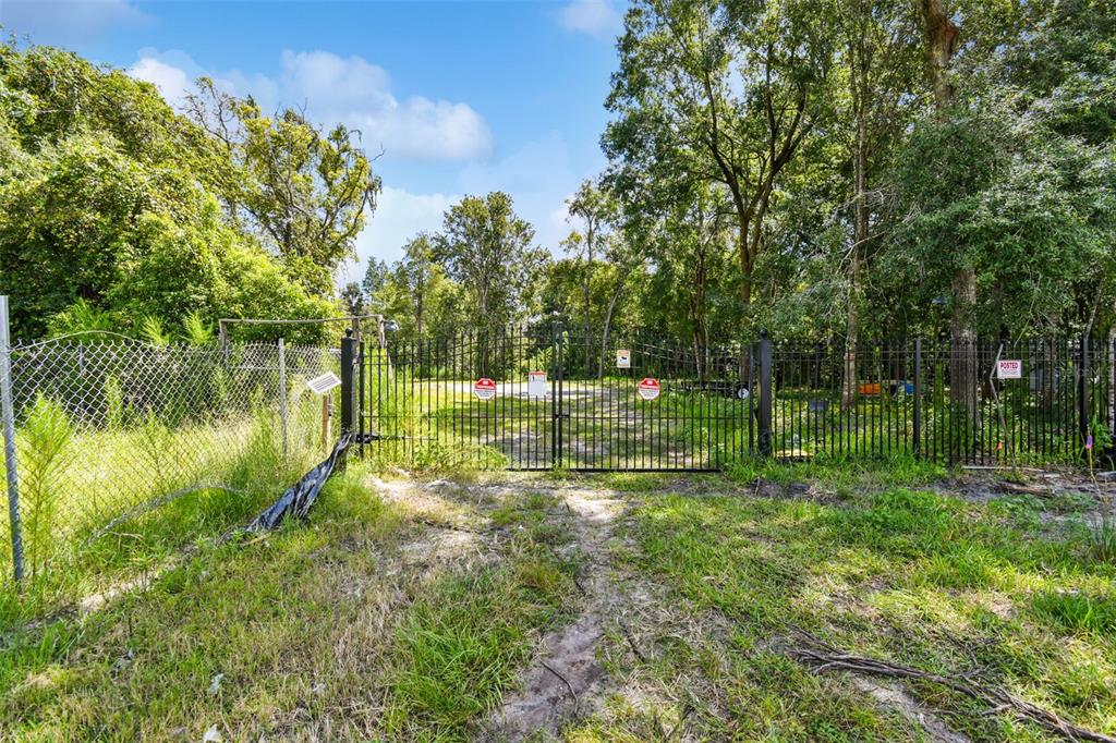 A black metal gate secures the entrance to a wooded lot with a dirt path — 1758 LAND O LAKES BOULEVARD, LUTZ, FL