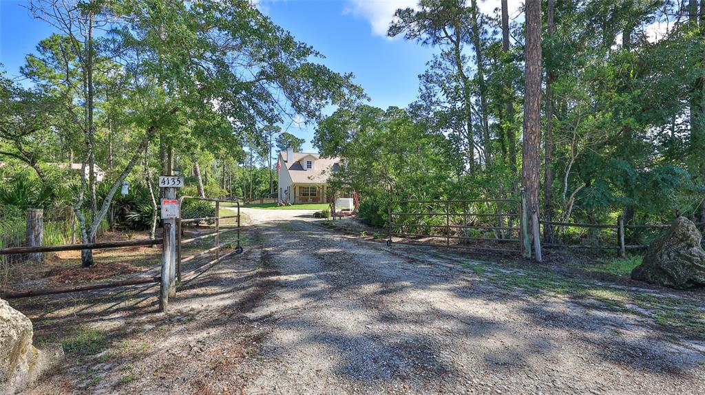 A gravel driveway leads through an open metal gate toward a house surrounded by trees — 4135 QUAIL RANCH ROAD, NEW SMYRNA BEACH, FL