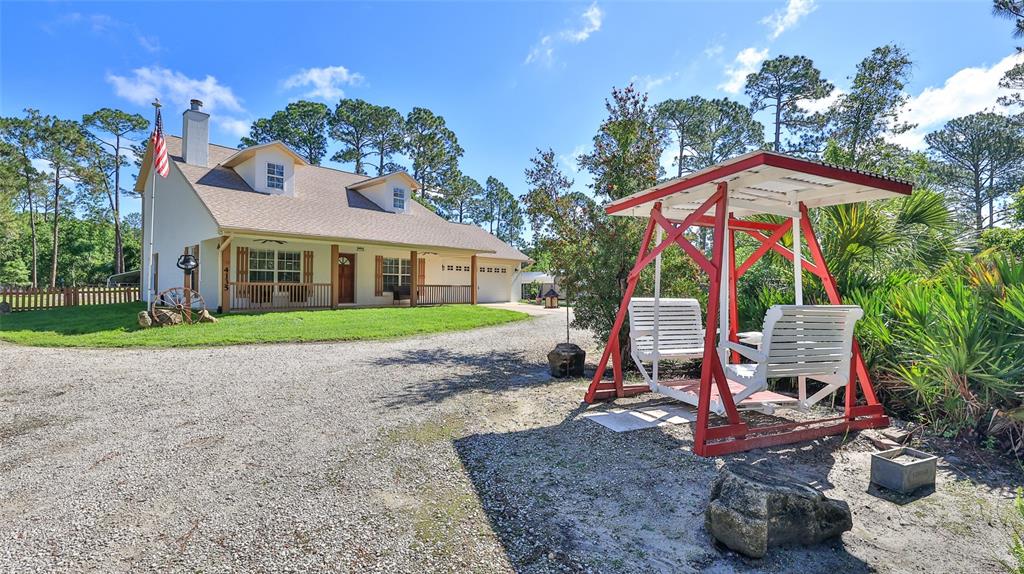A two-story house with a gravel driveway and a red-framed porch swing in the foreground — 4135 QUAIL RANCH ROAD, NEW SMYRNA BEACH, FL