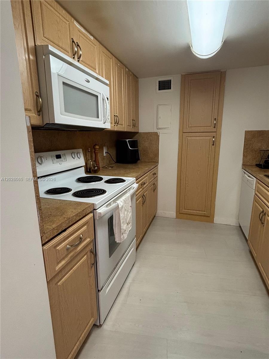 A galley kitchen features light wood cabinets, white appliances, and brown laminate countertops — 900 Bay Dr # 811, Miami Beach FL 33141, MIAMI BEACH, FL