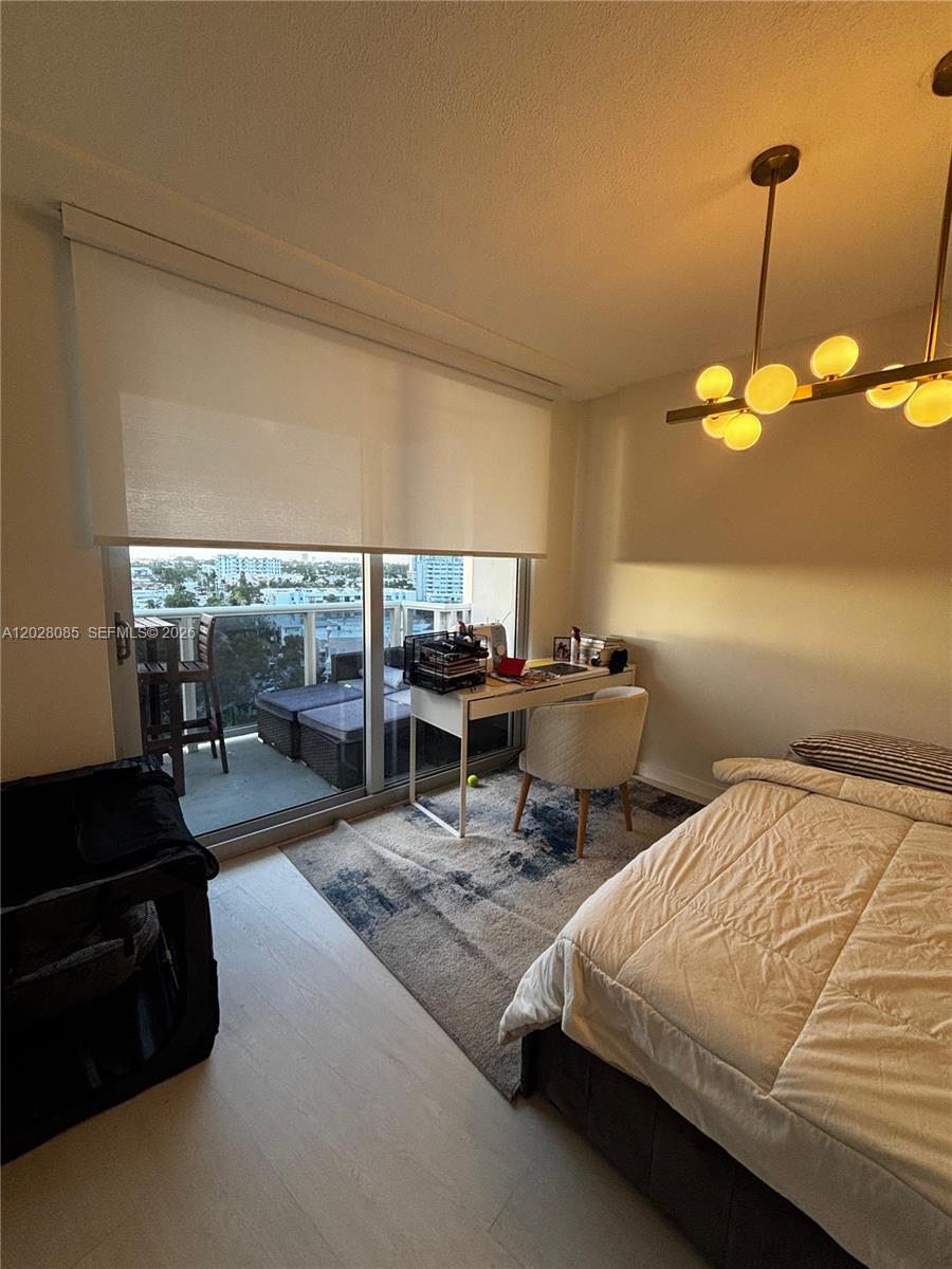 A bedroom features a desk, a bed, a modern light fixture, and a balcony view — 900 Bay Dr # 811, Miami Beach FL 33141, MIAMI BEACH, FL
