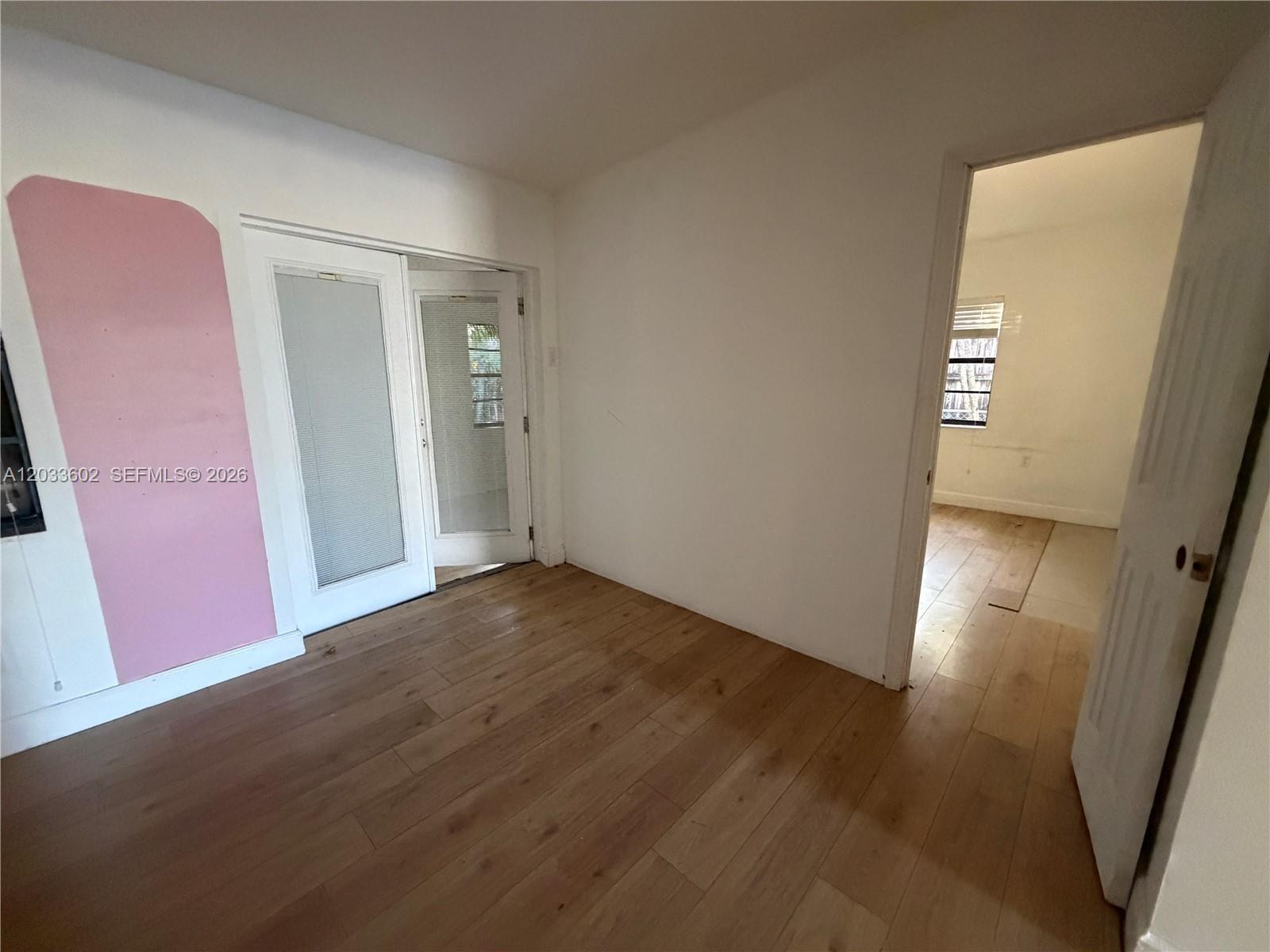An interior room features light wood-look flooring, a pink accent wall, and a doorway leading outside — 1080 NE 83rd St, Miami FL 33138, MIAMI, FL