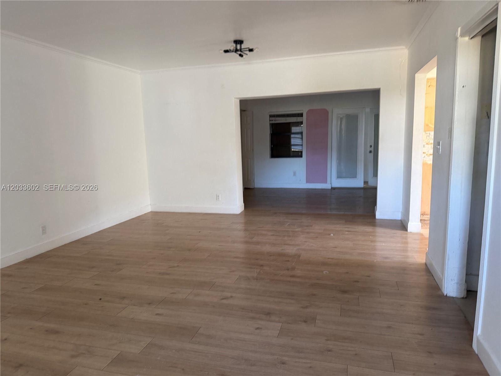 An empty room with light wood-look flooring and white walls leads into an adjacent space — 1080 NE 83rd St, Miami FL 33138, MIAMI, FL