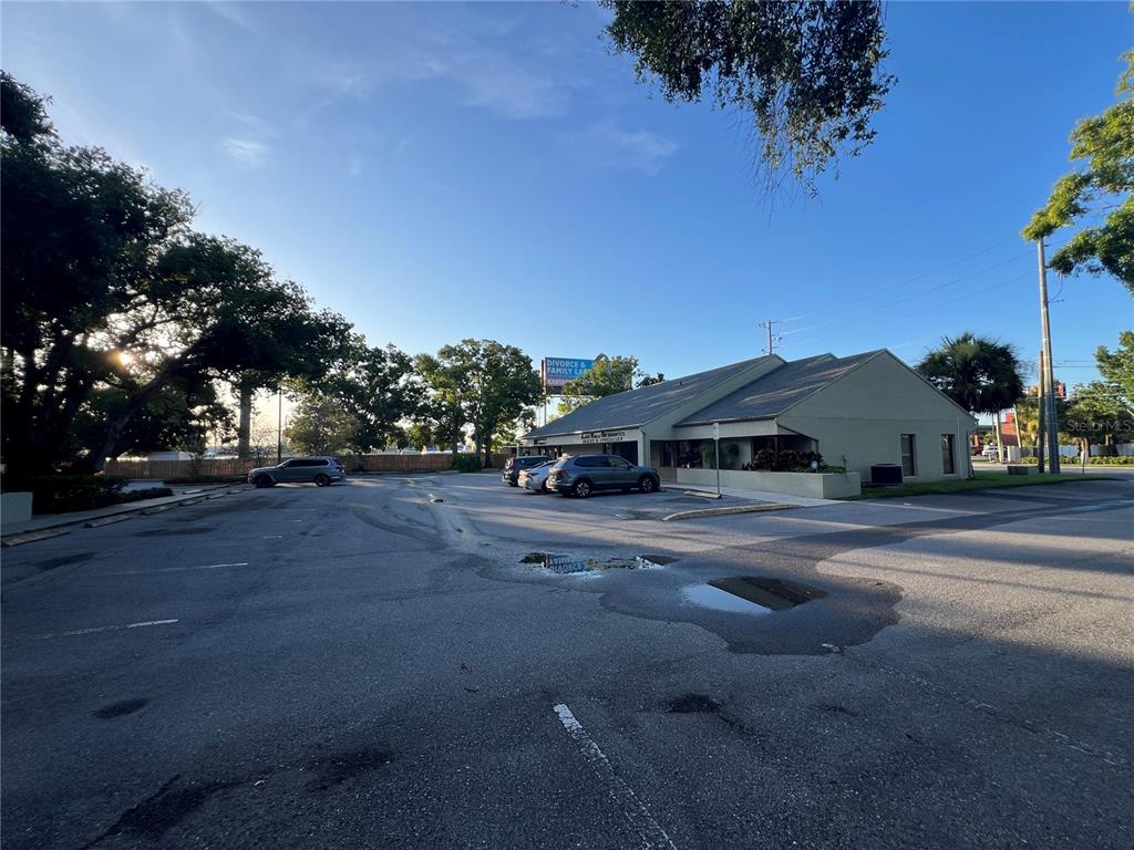 A low-rise commercial building sits behind a large, paved parking lot with scattered puddles — 32502 US HIGHWAY 19 N UNIT B, PALM HARBOR, FL